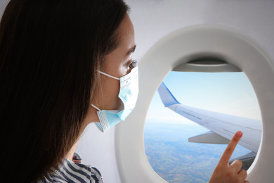 Image of Traveling by airplane during coronavirus pandemic. Woman with face mask near porthole