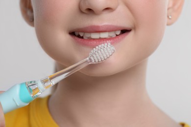 Photo of Girl brushing her teeth with electric toothbrush on light grey background, closeup