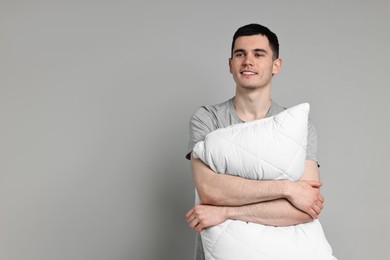 Photo of Happy man in pyjama holding pillow on grey background, space for text