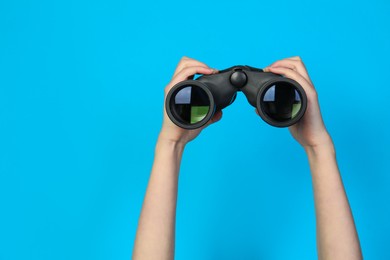 Photo of Woman holding modern binoculars on light blue background, closeup. Space for text