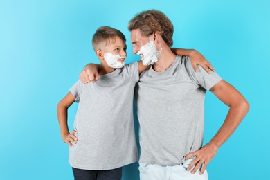 Photo of Father and son with shaving foam on faces against color background
