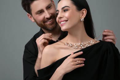 Photo of Man putting elegant necklace on beautiful woman against grey background, closeup