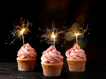 Image of Birthday cupcakes with sparklers on table against dark background