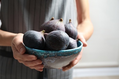 Photo of Woman holding bowl with fresh ripe figs on light background