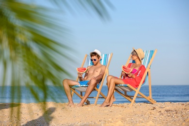 Photo of Young couple with watermelon slices in beach chairs at seacoast