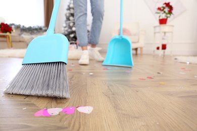 Photo of Woman cleaning messy room after New Year party, focus on broom
