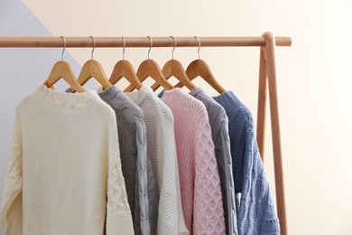 Photo of Collection of warm sweaters hanging on rack near color wall
