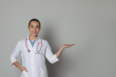 Photo of Beautiful young doctor showing something on light grey background