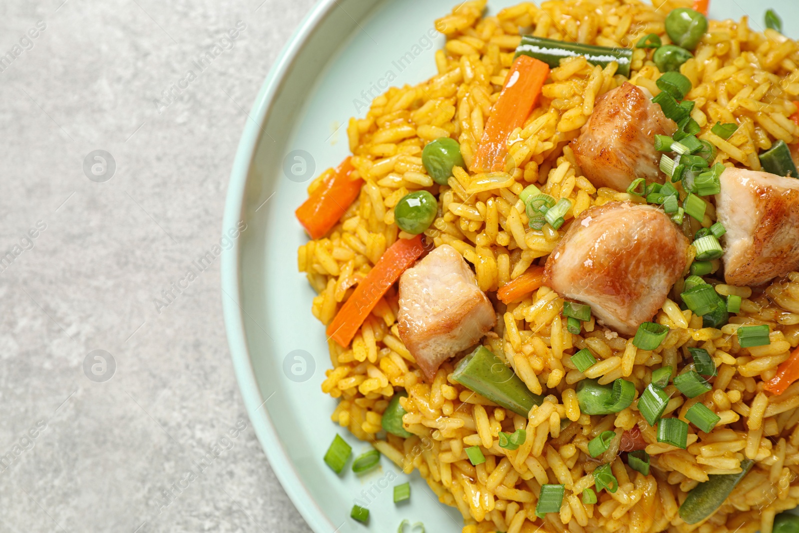 Photo of Delicious rice pilaf with vegetables and chicken on light grey table, closeup