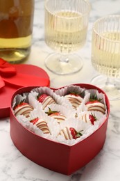 Photo of Delicious chocolate covered strawberries in heart shaped box and sparkling wine on white marble table