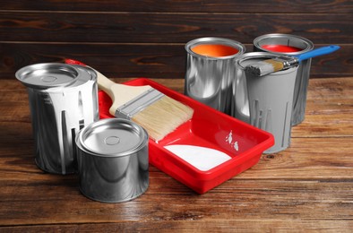 Photo of Cans of paints, brushes and tray on wooden table