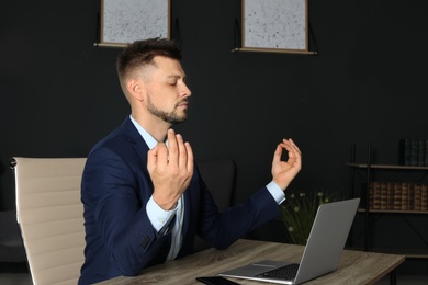 Photo of Businessman practicing zen yoga at table in office
