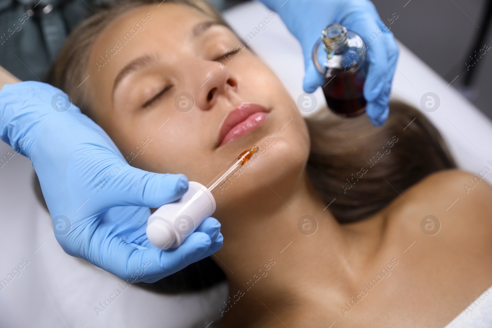 Photo of Cosmetologist applying serum on client's face in salon