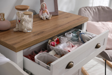 Photo of Modern open chest of drawers with baby clothes and accessories in room