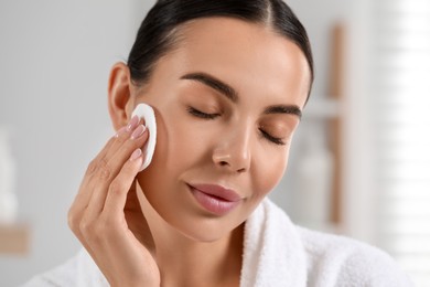 Photo of Beautiful woman removing makeup with cotton pad indoors, closeup