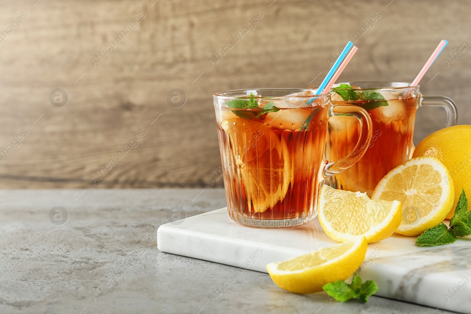 Photo of Cups of refreshing iced tea on table against wooden background. Space for text