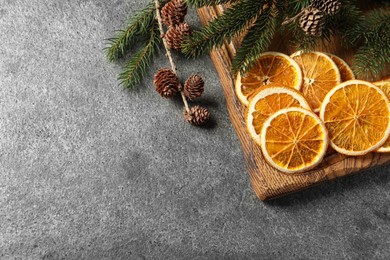 Photo of Dry orange slices, cones and fir tree branches on grey table, space for text