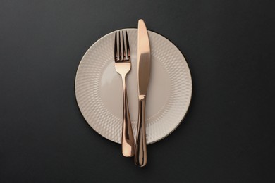 Photo of Clean plate, fork and knife on black table, top view