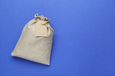 Photo of Tied burlap bag with tag on blue background, top view. Space for text
