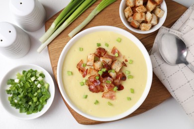 Photo of Tasty potato soup with bacon, green onion and croutons in bowl served on white table, flat lay