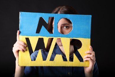 Photo of Young woman holding poster in colors of Ukrainian flag with words No War on black background
