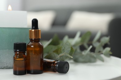 Photo of Aromatherapy. Bottles of essential oil, burning candle and eucalyptus leaves on white table