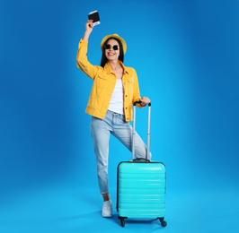 Photo of Beautiful woman with suitcase and ticket in passport for summer trip on blue background. Vacation travel