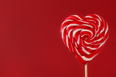 Photo of Sweet heart shaped lollipop on red background, closeup view with space for text. Valentine's day celebration