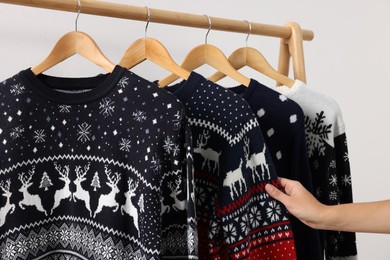 Photo of Woman choosing Christmas sweater from rack near white wall, closeup