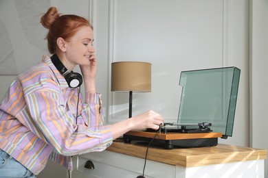 Photo of Beautiful young woman using turntable at home