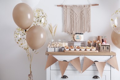 Photo of Baby shower party. Different delicious treats on white wooden chest of drawers and decor near light wall