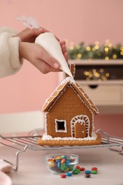 Photo of Woman decorating gingerbread house with icing at table, closeup
