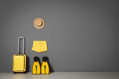 Photo of Suitcase with hat and swim fins near gray wall. Space for text