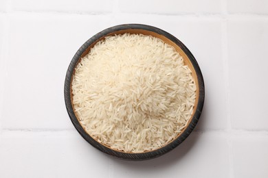 Photo of Raw basmati rice in bowl on white tiled table, top view