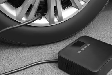 Photo of Inflating car tire with portable air pump outdoors, closeup