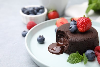 Photo of Plate with delicious chocolate fondant, berries and mint on grey table, closeup. Space for text