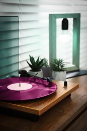 Image of Stylish turntable with vinyl record on wooden chest of drawers indoors