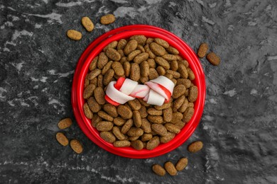 Photo of Dry dog food and treat (knotted chew bone) on black textured background, top view