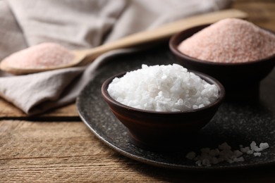 Photo of Different salt in bowls on wooden table, closeup. Space for text