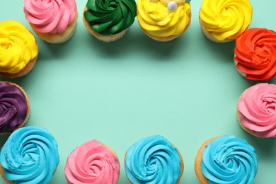 Photo of Frame of delicious cupcakes with bright cream on turquoise background, flat lay. Space for text