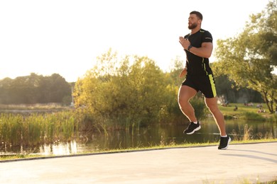 Photo of Young man running near pond in park. Space for text
