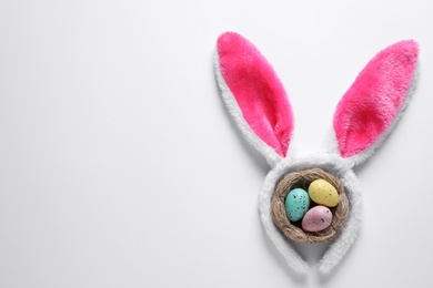 Photo of Headband with bunny ears and painted eggs on white background, top view. Easter holiday