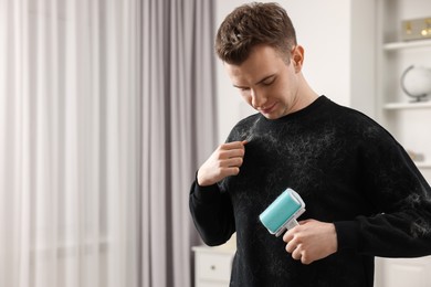 Photo of Pet shedding. Man with lint roller removing dog's hair from sweater at home. Space for text