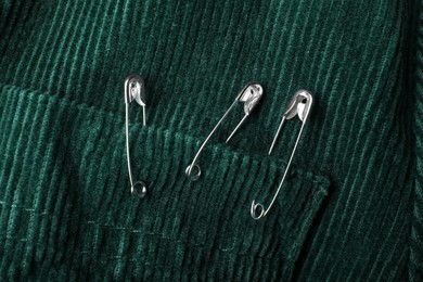Photo of Metal safety pins on green fabric, closeup