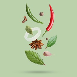 Image of Different spices falling on light green background