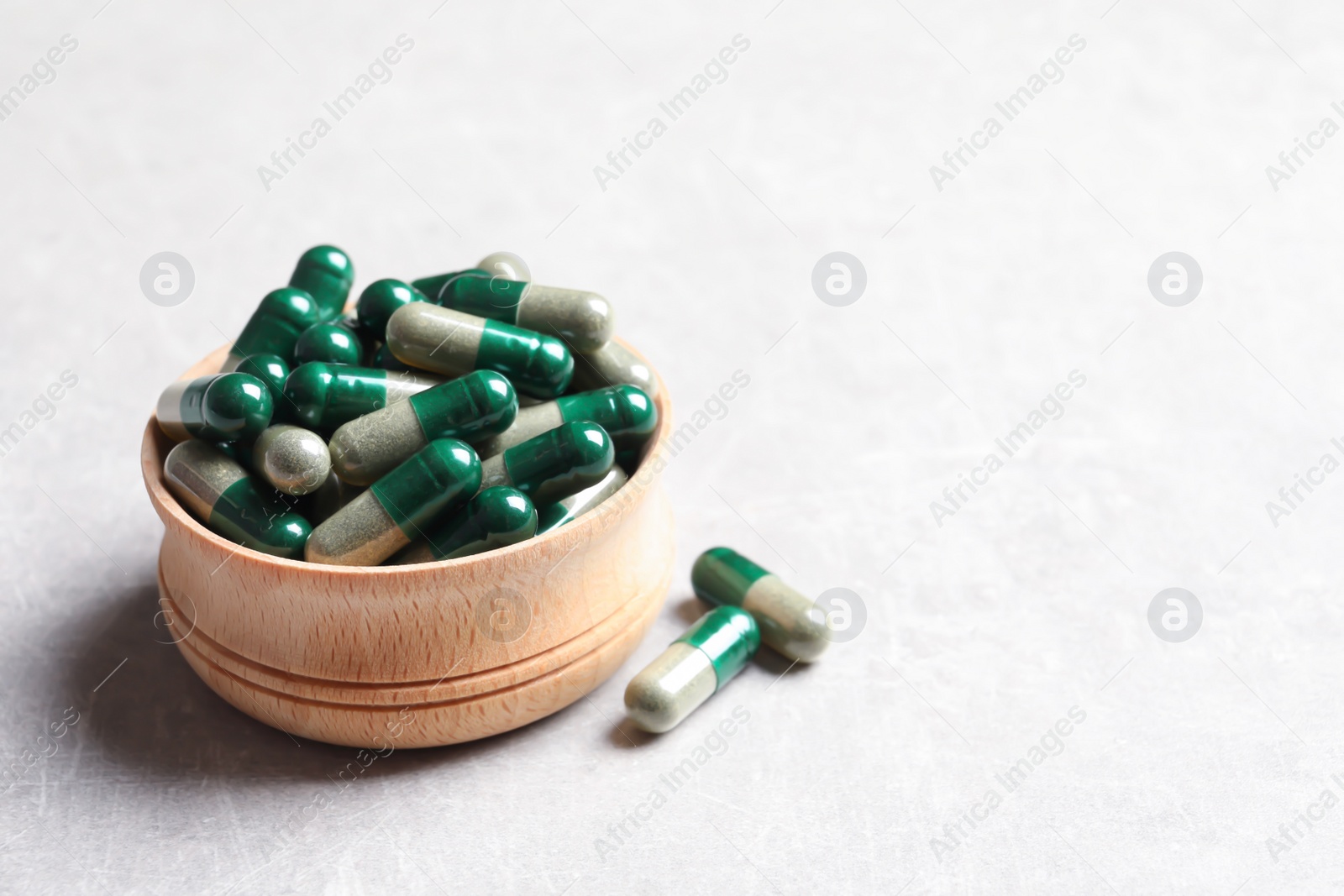 Photo of Wooden bowl with green spirulina capsules on light table, space for text