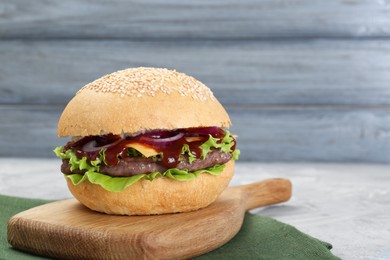 Delicious cheeseburger with lettuce, onion, ketchup and patty on grey table, closeup. Space for text