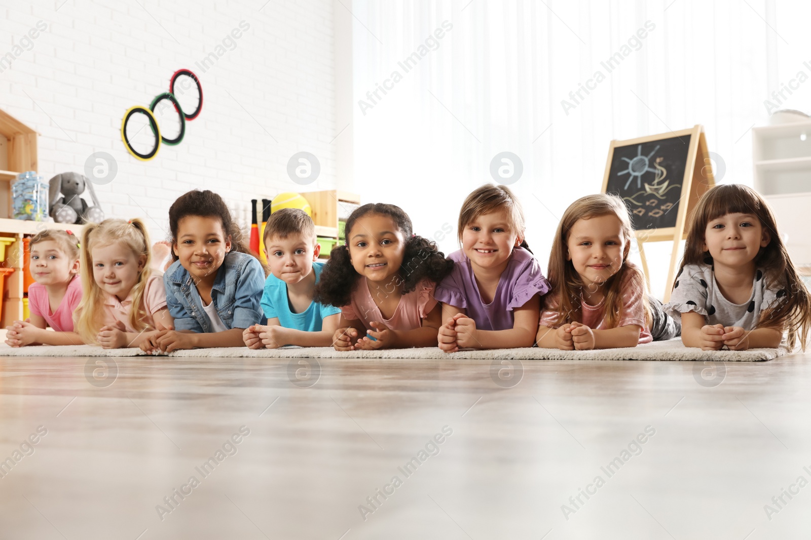 Photo of Group of cute little children lying on floor indoors. Kindergarten playtime activities