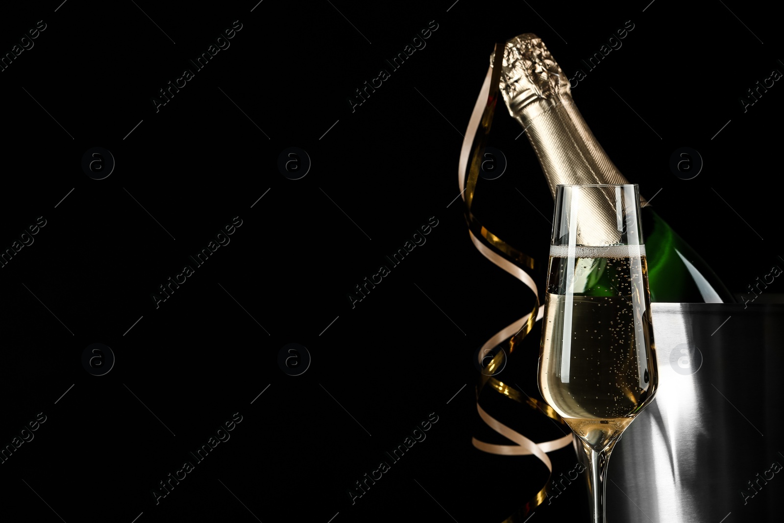 Photo of Glass of champagne near bucket with bottle on black background, space for text