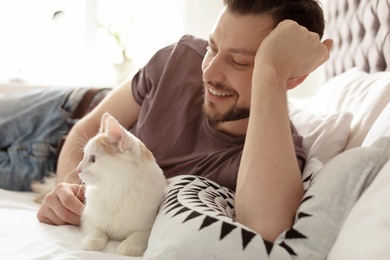 Photo of Young man with cute cat on bed at home